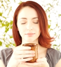 Close-up of a beautiful woman with eyes closed holding a cup of herbal tea