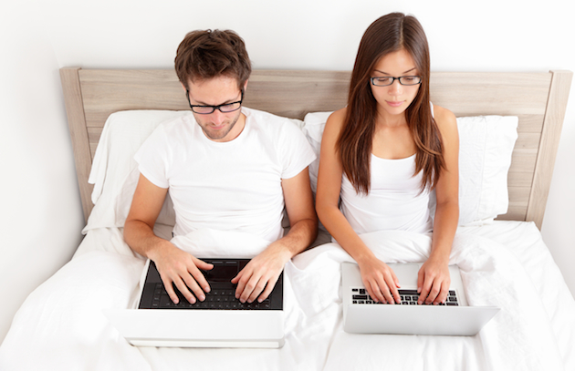 Couple working on laptops in bed